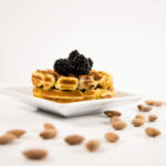 Side view - Two Blackberry Almond Chaffle on a white plate, topped with blackberries and surrounded by whole almonds.