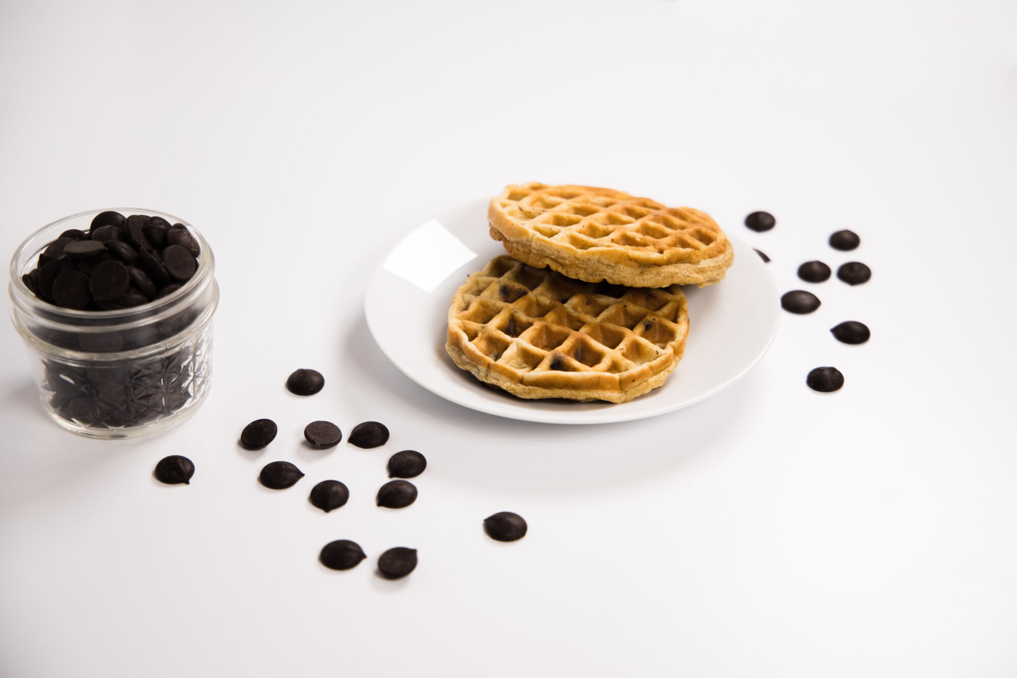 Two Chocolate Chip Chaffles on a white plate surrounded by chocolate chips.
