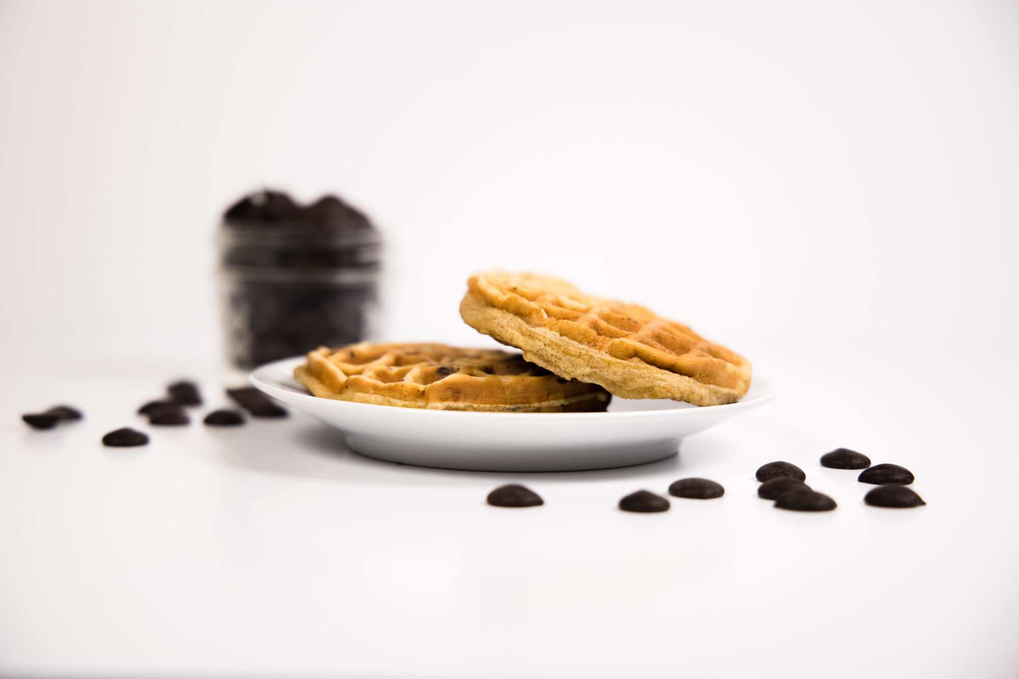 Side view - Two Chocolate Chip Chaffles on a white plate surrounded by chocolate chips.