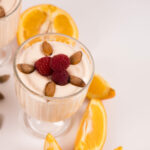 Top view - single dessert cup filled with Mango Orange Yogurt, topped with almonds and raspberries. Sliced oranges on the side.