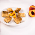 Peaches and Cream Crumb Bars on a white plate with slices of fresh peaches.