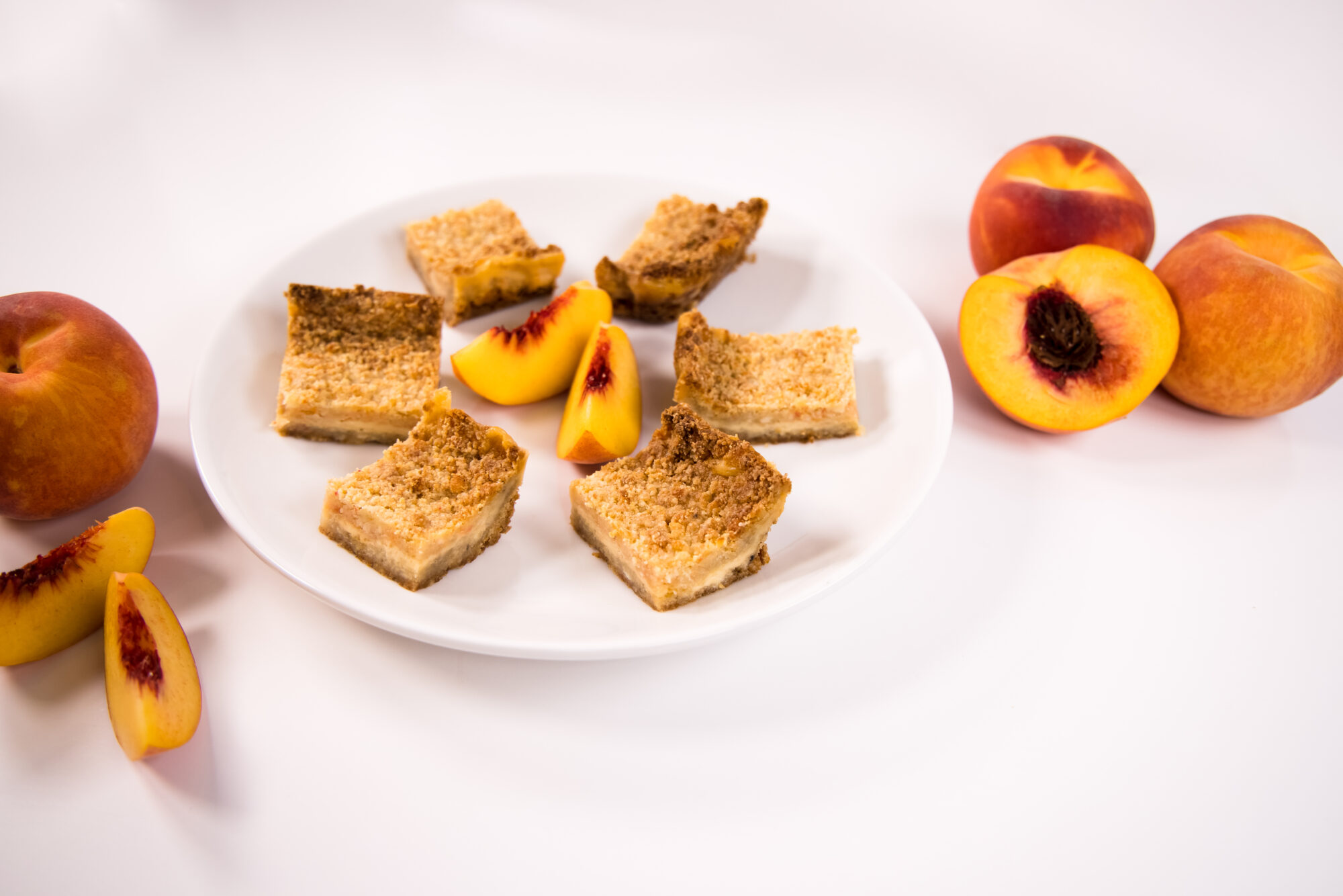 Peaches and Cream Crumb Bars on a white plate with slices of fresh peaches.
