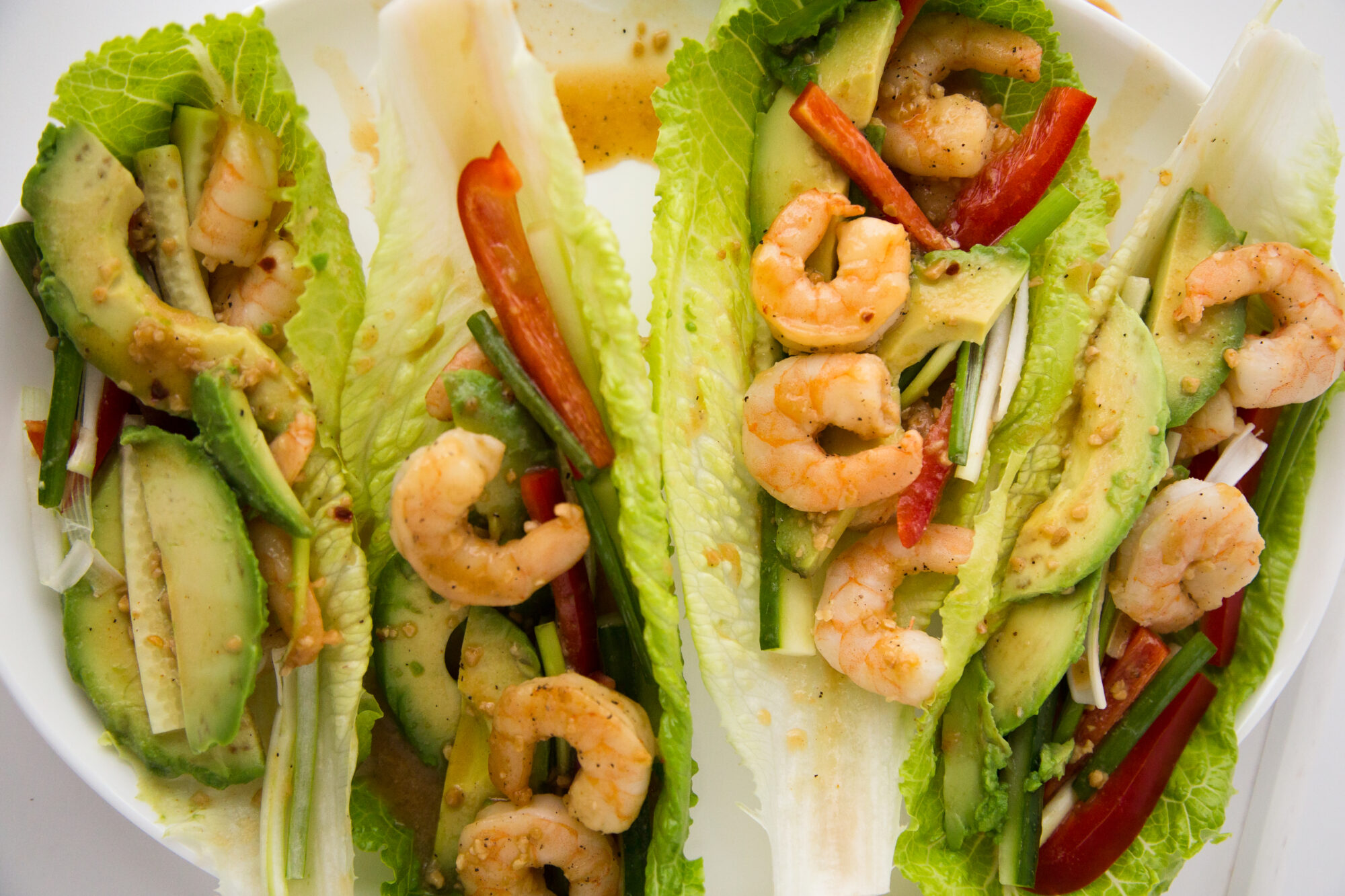Close up - Lettuce leaves topped with spicy shrimp, sliced avocado and red peppers.