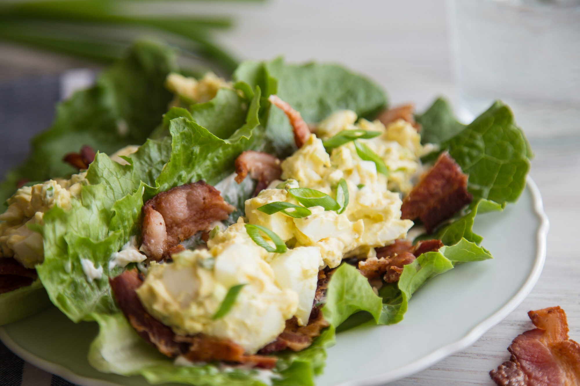 Close up of egg salad on top of bacon slices, lying on a lettuce leaf