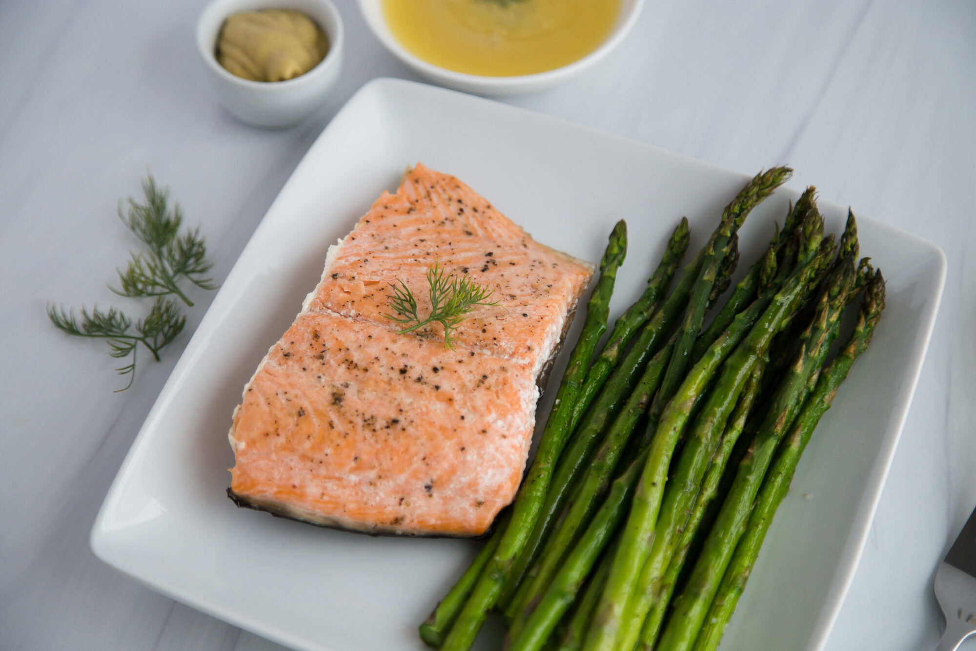 Asparagus spears and salmon on white plate. Side dish of dipping sauce.