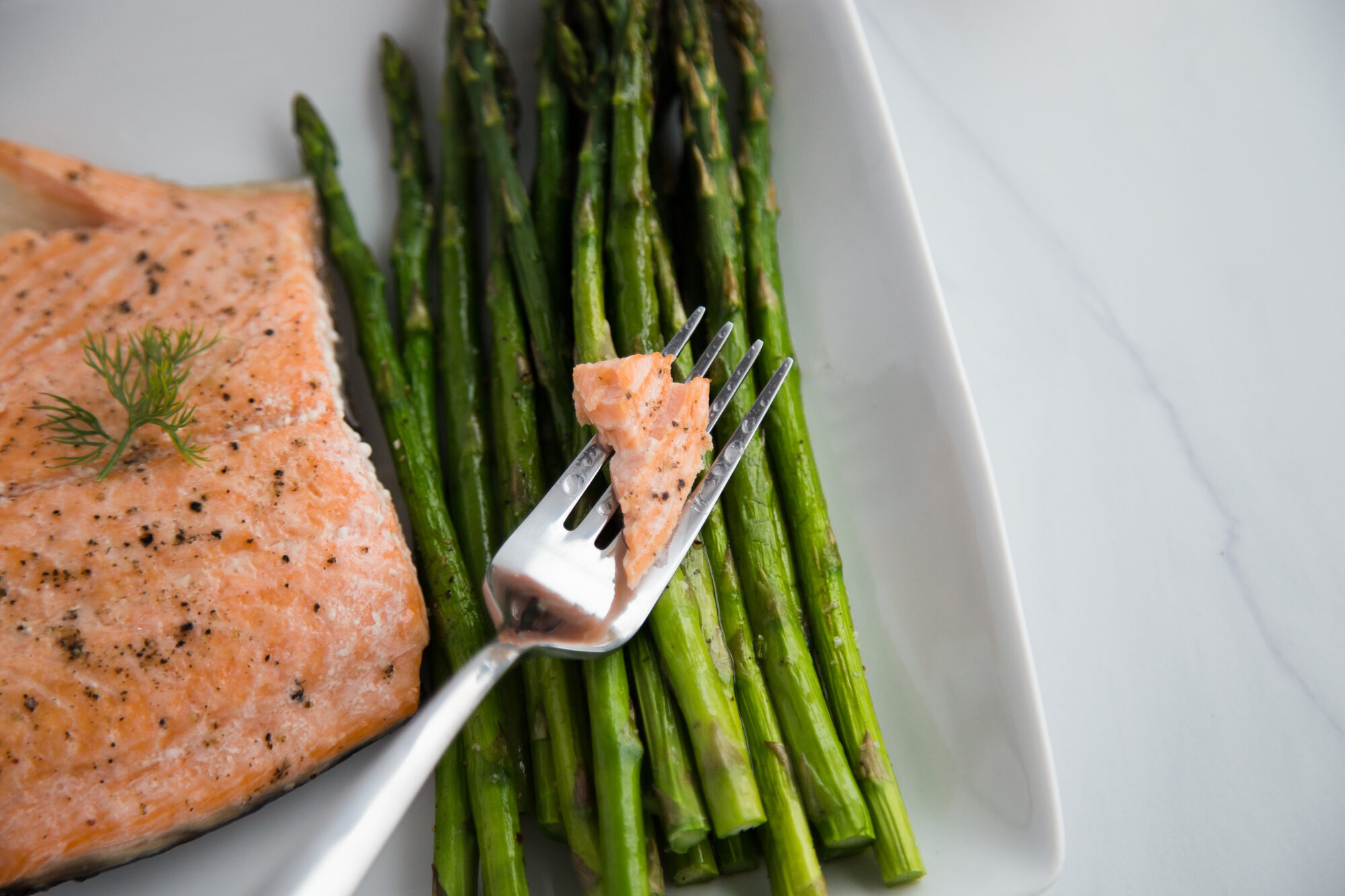 Close up-salmon and asparagus spears on a white plate and a fork with a piece of salmon.