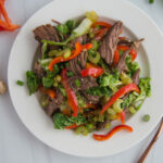 Top view of sliced beef, red peppers, celery and other veggies on a white plate