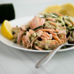 Close up of salmon and zucchini noodles on a white plate with a lemon wedge and a fork