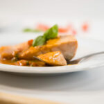 Close up - Salmon with tomato basil sauce on a white plate with a fork.