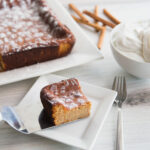 Piece of ginger cake on a spatula. A bowl of chantilly cream to the side, along with the rest of the Ginger Cake.