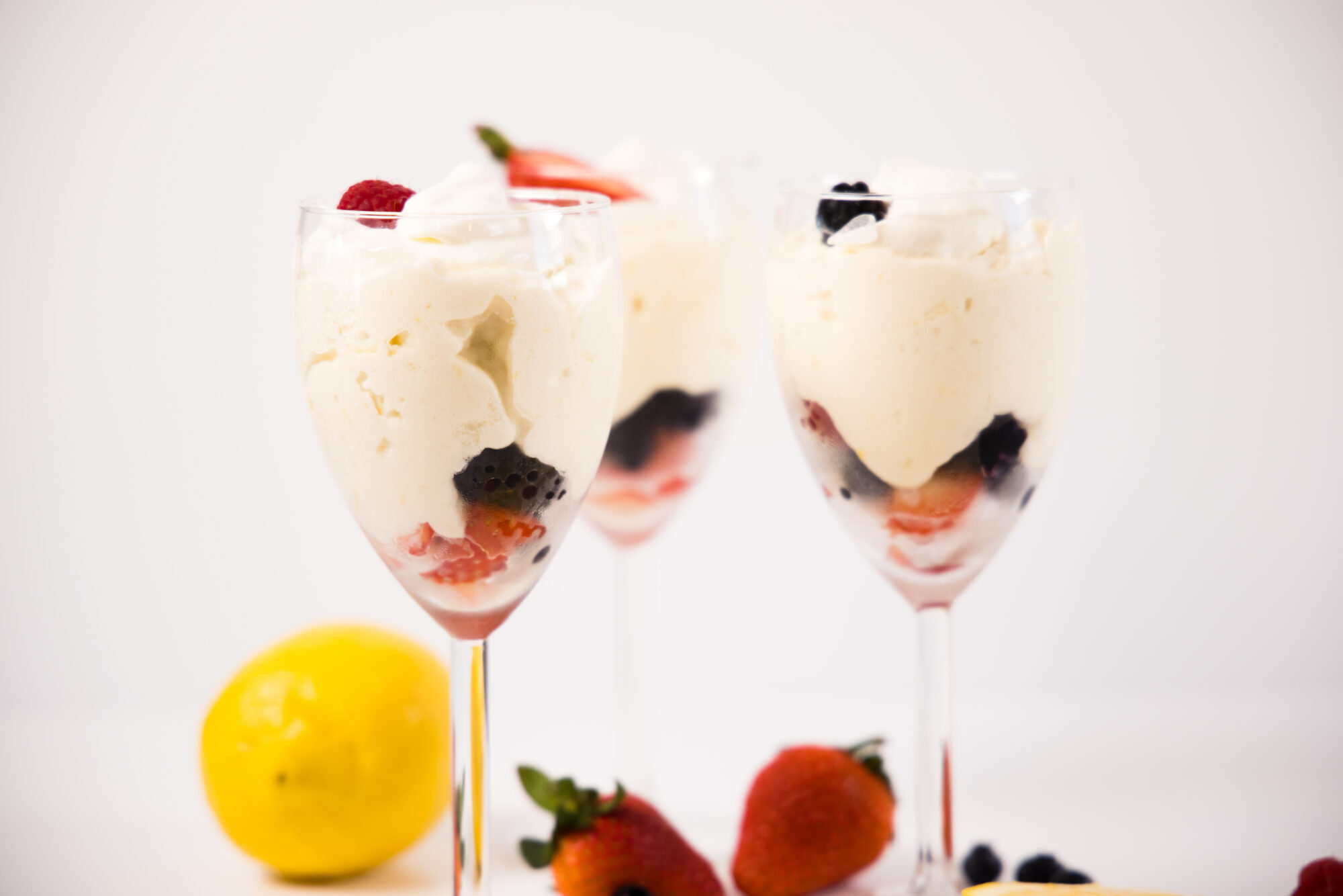 Close up - Three glass goblets filled with berries and Lemon Mousse. Surrounded by berries and lemons.