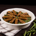 Close up of dish with green beans and sausages on top