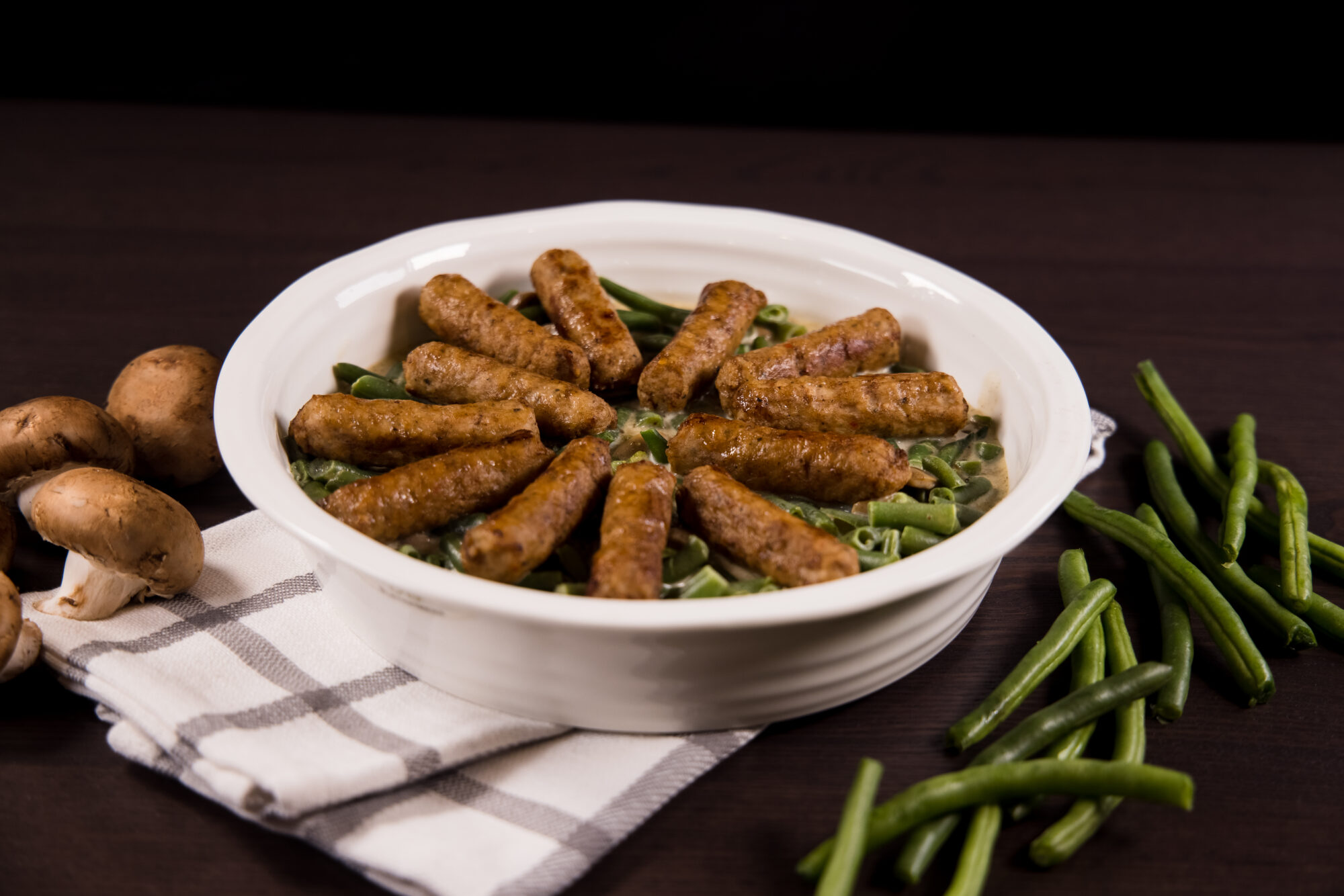 Close up of dish with green beans and sausages on top
