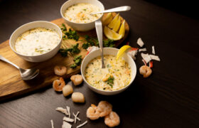 Three white bowls filled with Seafood Bisque. Lemon wedges and shrimp on the side.