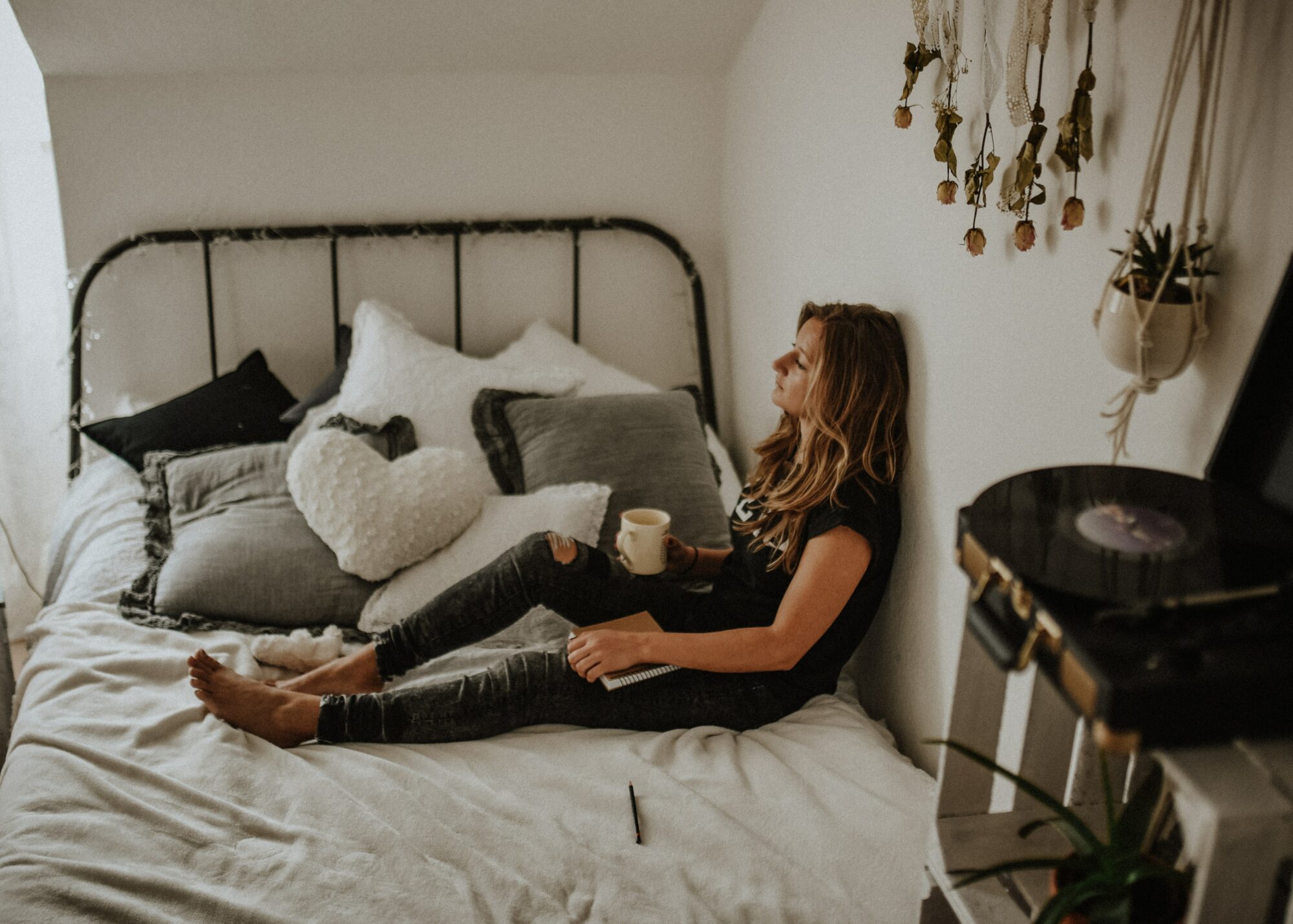 tired woman holding coffee cup and notebook on bed