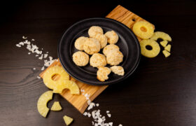 Black plate filled with Coconut Macaroons. Sliced pineapple on the side.