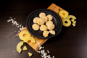 Black plate filled with Coconut Macaroons. Sliced pineapple on the side.