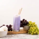 Side view - Purple Cow Float in tall glass, with two straws, surrounded by grapes.