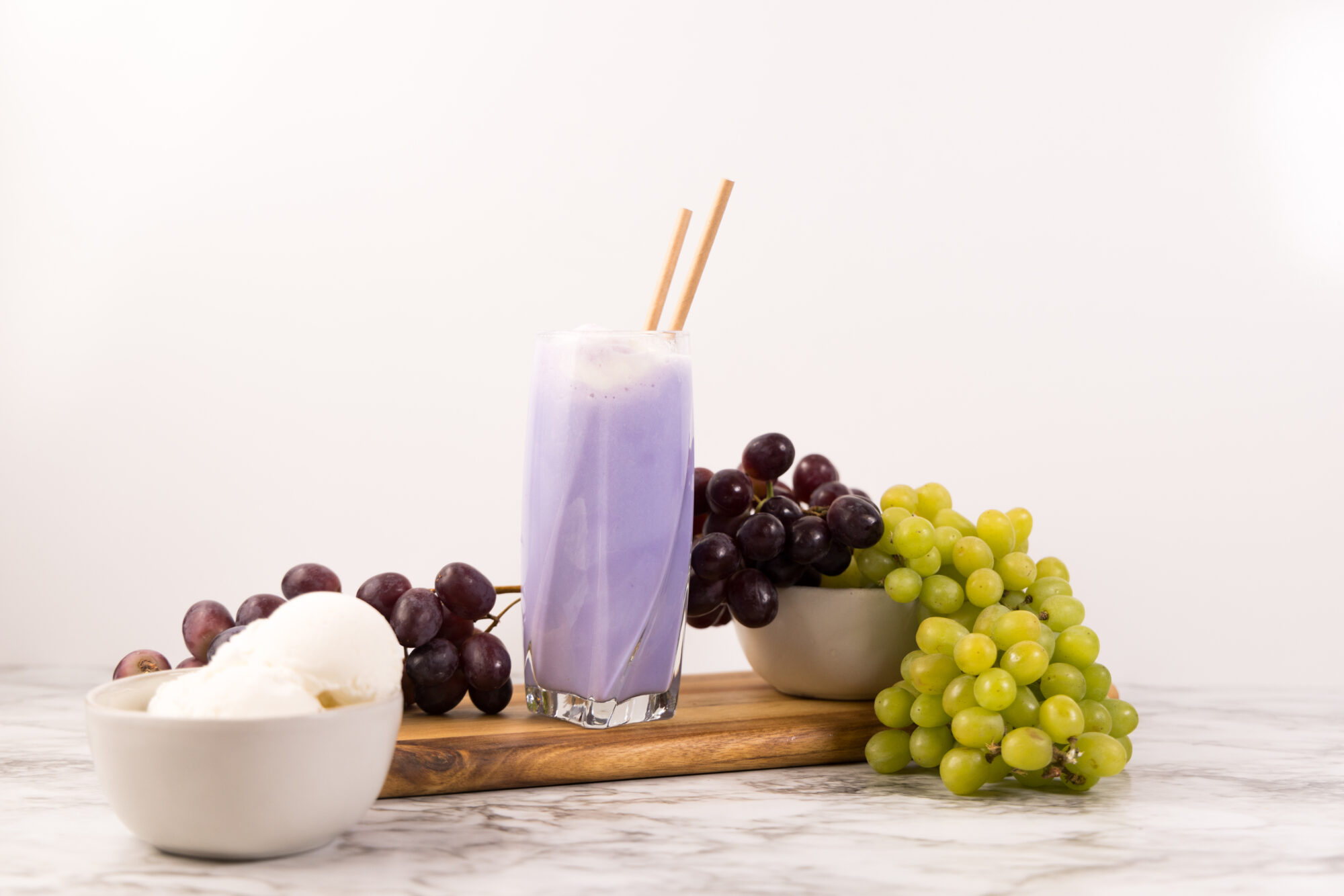 Side view - Purple Cow Float in tall glass, with two straws, surrounded by grapes.