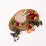 Top view - Tall glass filled with a Strawberry Mint Smoothie. Surrounded by strawberries and chocolate pieces.