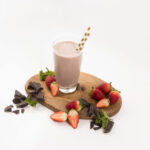 Tall glass filled with a Strawberry Mint Smoothie. Surrounded by strawberries and chocolate pieces.