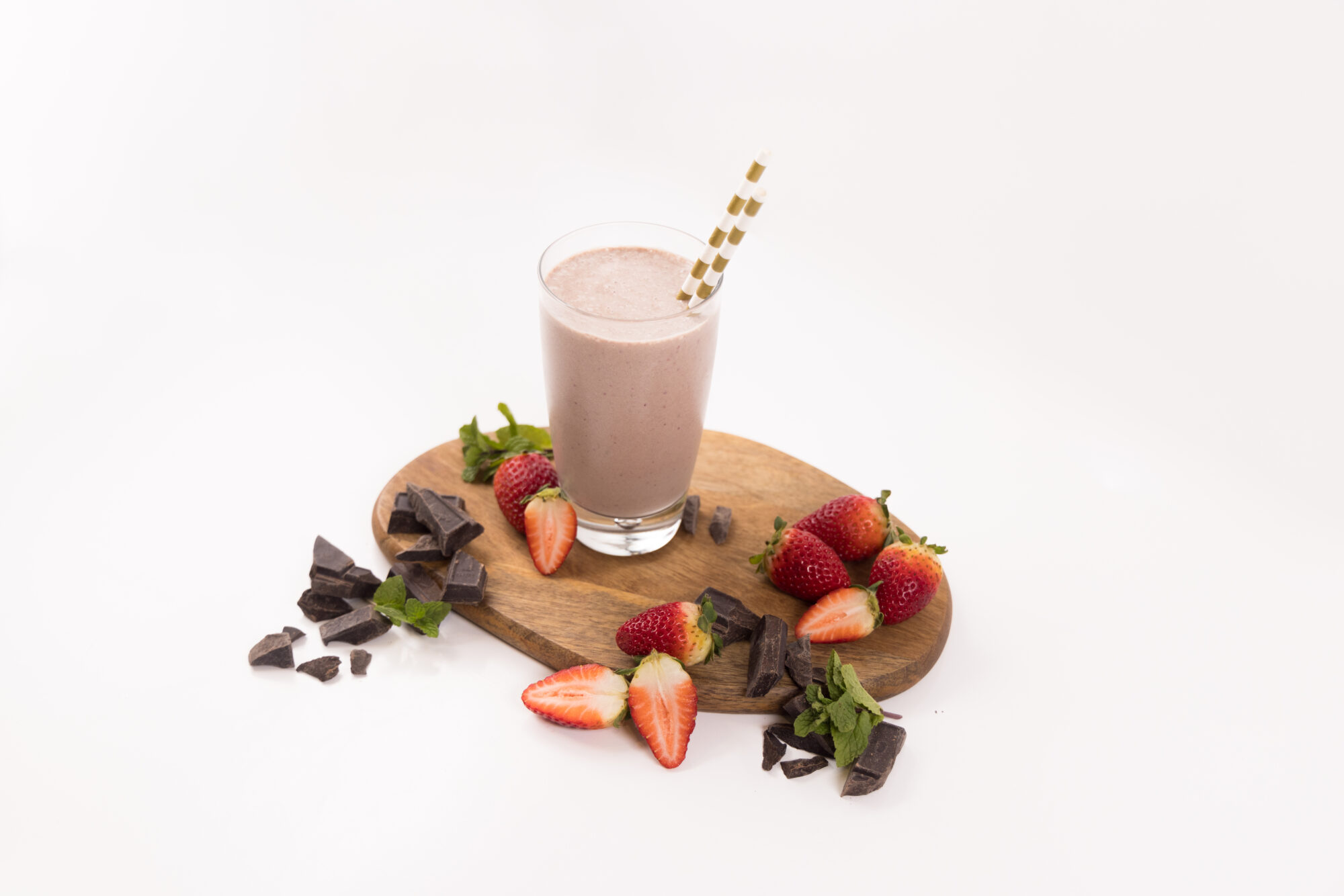 Tall glass filled with a Strawberry Mint Smoothie. Surrounded by strawberries and chocolate pieces.